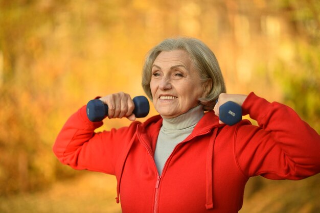 Gelukkig fit senior vrouw trainen in herfst park met halters