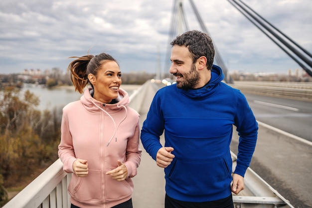 Gelukkig fitte sportieve heteroseksuele vrienden die op de brug rennen en chatten. Outdoor fitness op bewolkt weer concept. Stadsleven.