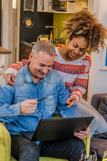 Gelukkig gemengd ras paar online winkelen in het comfort van hun huis. Paar genieten van online winkelen op de bank zitten.