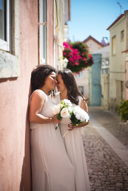 Gelukkig getrouwde vrouwen teder knuffelen in straat. liefdevolle vrouwen in trouwjurken met boeketten die teder knuffelen