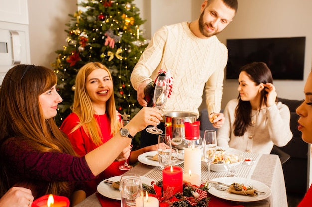 gelukkig gezelschap van vrienden die het nieuwe jaar vieren met champagne aan tafel bij de versierde kerstboom