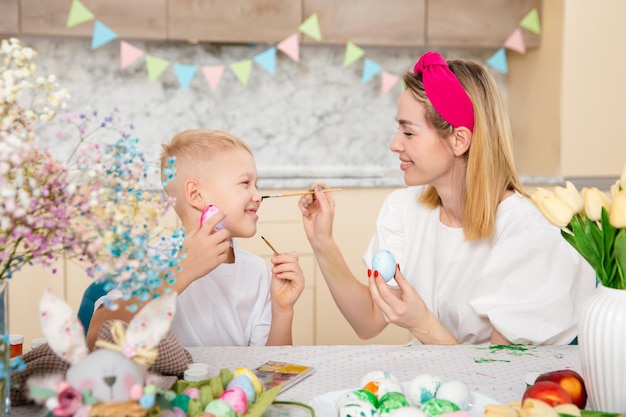 Foto gelukkig gezin bereidt zich voor op pasen schattig kind met moeder die eieren schildert thuisactiviteit concept van eenheid en liefde moeder en zoon