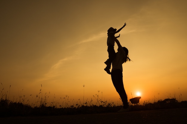 gelukkig gezin. Een moeder en een zoon die op grasgebieden in openlucht bij avondsilhouet spelen