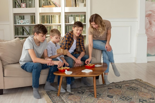 Gelukkig gezin, een vrouw en drie tienerjongens zitten op de bank in de woonkamer en eten fastfood in het rood