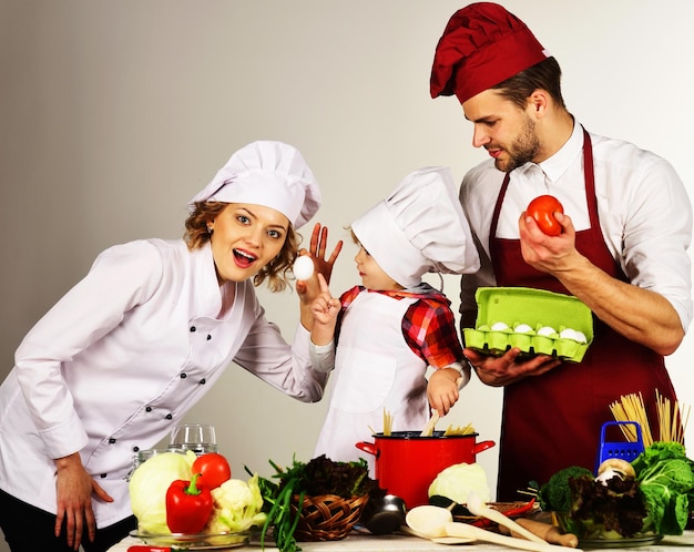 Gelukkig gezin in de keuken schattig kind en ouders in koksmuts moeder en vader leren zoon koken