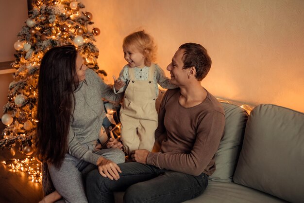 Gelukkig gezin met een kind thuis in de buurt van de kerstboom wachten op het nieuwe jaar