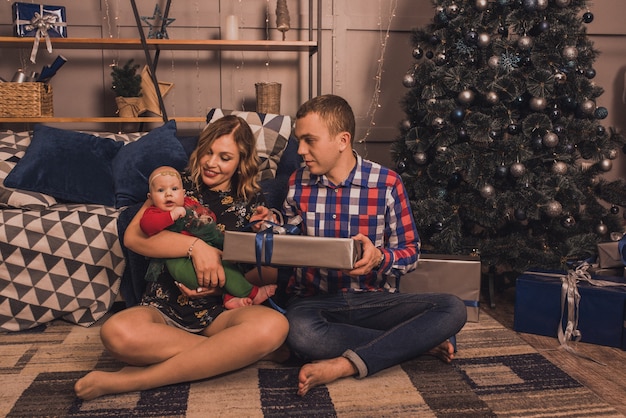 Gelukkig gezin met kind dat Nieuwjaar en Kerstmis viert bij versierde kerstboom en slingers