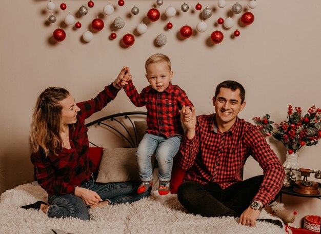 Gelukkig gezin met kind dat Nieuwjaar en Kerstmis viert bij versierde kerstboom en slingers