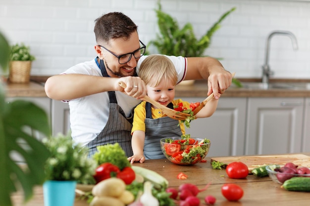 Gelukkig gezin met kind dat thuis groentesalade bereidt