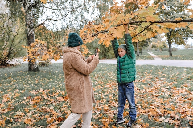 Gelukkig gezin moeder en zoon spelen en lachen tijdens herfstwandeling Moeder maakt foto's van haar zoon aan de telefoon bij de esdoorn