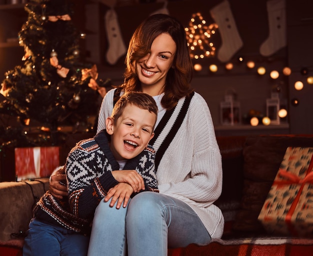 Gelukkig gezin. Mooie moeder en haar schattige kleine jongen zitten samen op de bank in een versierde kamer tijdens de kerstperiode.