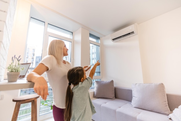 Gelukkig gezin onder airconditioner, moeder met afstandsbedieningschakelaar op airconditioning in woonkamer pas comforttemperatuur aan voor dochter, klimaatsysteem in modern huis