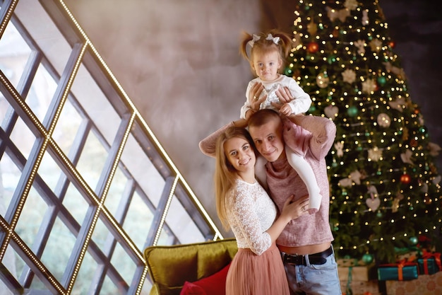 Gelukkig gezin samen in gezellig interieur in de buurt van feestelijke kerstboom Openhartig waar moment Jong gezin met klein babymeisje Gelukkig ouderschap Goed humeur en samen plezier maken