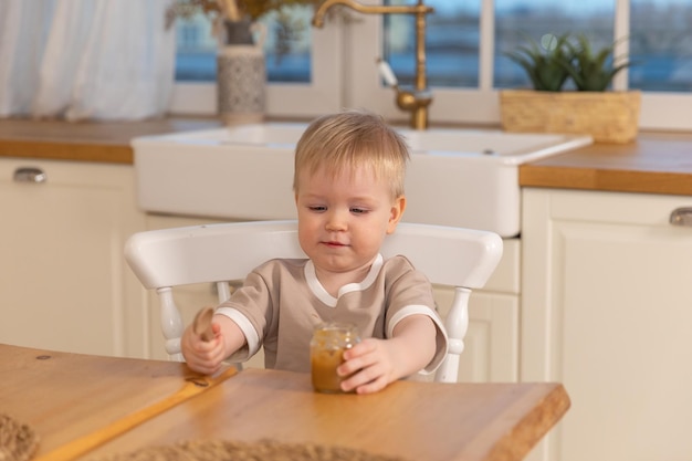 Gelukkig gezin thuis babyjongen die zichzelf voedt in de keuken kleine jongen met een rommelig grappig gezicht eet gezondheid