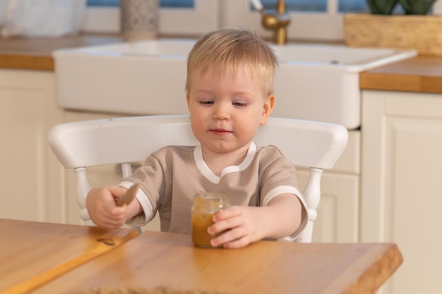 Gelukkig gezin thuis babyjongen die zichzelf voedt in de keuken kleine jongen met een rommelig grappig gezicht eet gezondheid