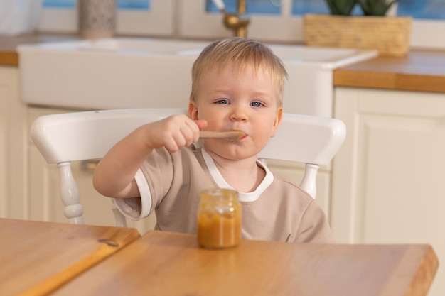 Gelukkig gezin thuis babyjongen die zichzelf voedt in de keuken kleine jongen met een rommelig grappig gezicht eet gezondheid