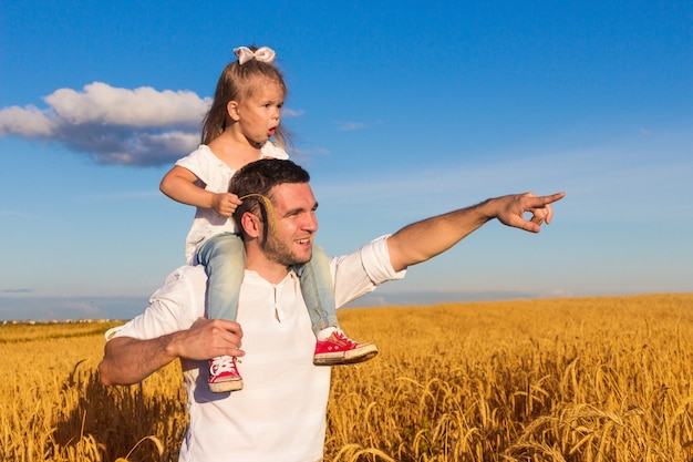 Gelukkig gezin. Vader en dochter zitten op zijn schouders staan in het midden van een tarweveld op een zonnige zomerdag