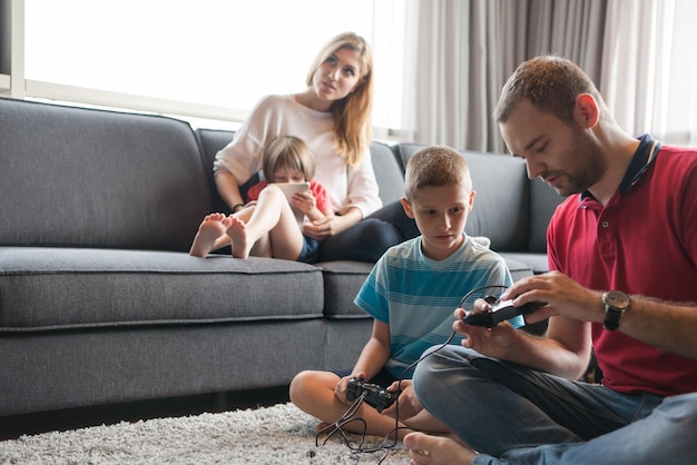 Gelukkig gezin. Vader, moeder en kinderen spelen een videogame Vader en zoon spelen samen videogames op de vloer