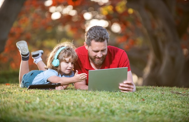 Gelukkig gezin van vader en zoon gebruiken laptop voor video-oproep of les, luister naar muziek in een koptelefoon op de familiedag in het park