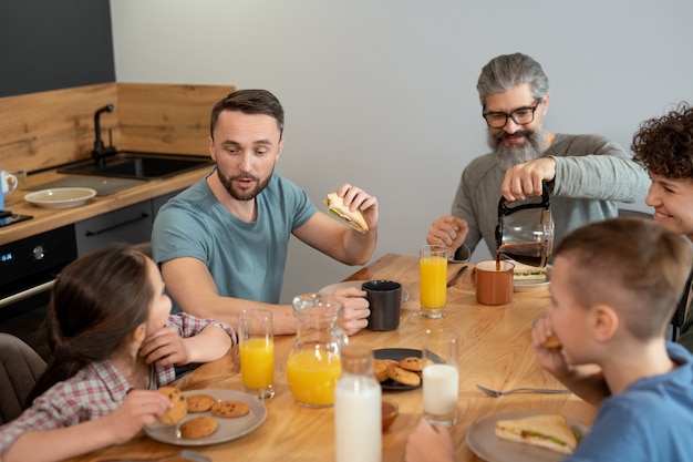 Gelukkig gezin van vijf zittend aan een tafel in de keuken en genietend van het ontbijt terwijl vader en dochter nieuwsgierige dingen bespreken