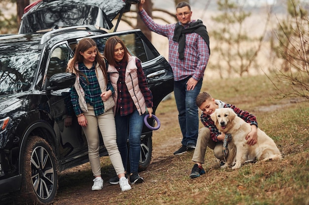 Gelukkig gezin veel plezier met hun hond in de buurt van moderne auto buiten in het bos