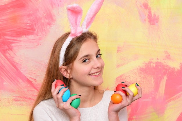 Gelukkig glimlachend klein tienermeisje met konijnenoren die geschilderde paaseieren houden. Gelukkig paasvakantie concept. Leuk meisje dat Pasen viert. Vrolijk kind met traditionele decoraties.
