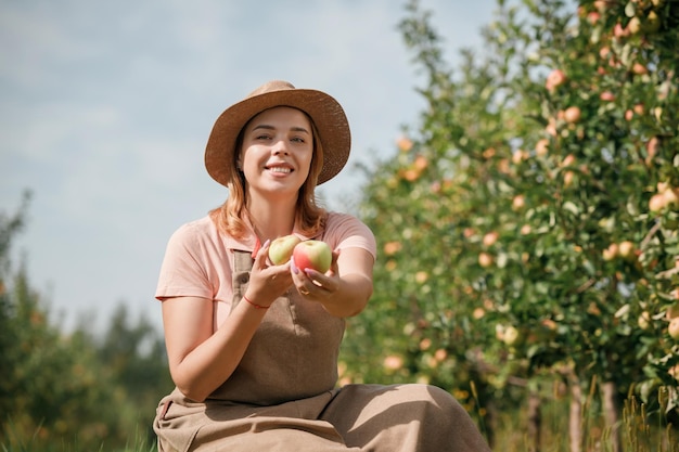 Gelukkig glimlachende vrouwelijke landbouwer die tijdens de herfstoogst verse rijpe appels plukt in de boomgaardtuin