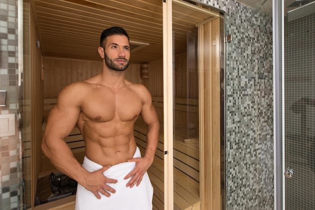 Gelukkig goed uitziende en aantrekkelijke jonge man met gespierd lichaam ontspannen in hete sauna