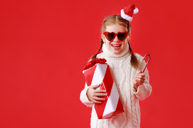 Gelukkig grappig kindmeisje met kerstcadeau op rood gekleurde achtergrond