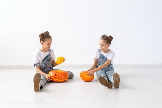 Gelukkig Halloween, vakantie en jeugdconcept - Schattige kleine tweelingzusjes meisjes met een pompoenen Jack-o'-lantern die plezier heeft terwijl ze tijd binnenshuis doorbrengt