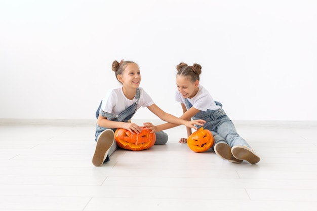 Gelukkig Halloween, vakantie en jeugdconcept - Schattige kleine tweelingzusjes meisjes met een pompoenen Jack-o'-lantern die plezier heeft terwijl ze tijd binnenshuis doorbrengt