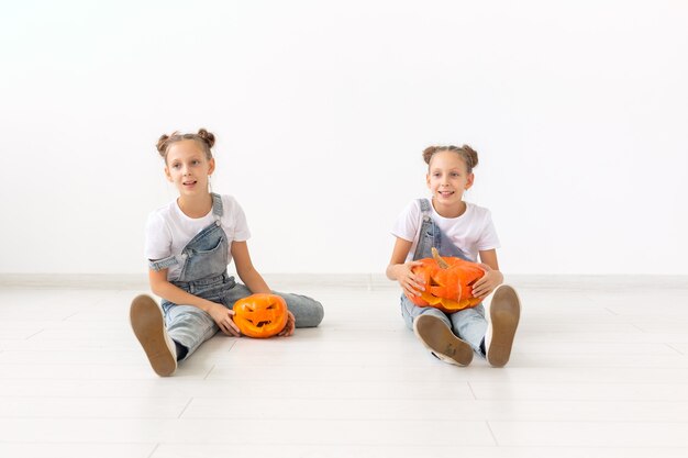 Gelukkig Halloween, vakantie en jeugdconcept - Schattige kleine tweelingzusjes meisjes met een pompoenen Jack-o'-lantern die plezier heeft terwijl ze tijd binnenshuis doorbrengt