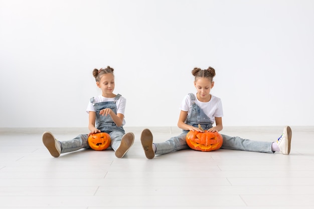 Gelukkig Halloween, vakantie en jeugdconcept - Schattige kleine tweelingzusjes meisjes met een pompoenen Jack-o'-lantern die plezier heeft terwijl ze tijd binnenshuis doorbrengt