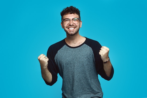 Gelukkig hipster man met baard dragen casual kleding en bril juicht geïsoleerd op blauwe achtergrond