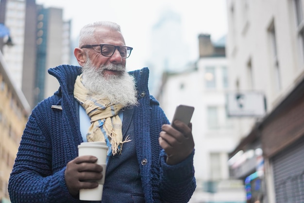 Gelukkig hipster senior zakenman met behulp van mobiele telefoon tijdens het drinken van koffie op winterdag