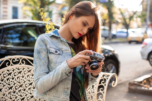 Gelukkig hipstermeisje die foto met retro camera op stadsstraat maken. Reisconcept