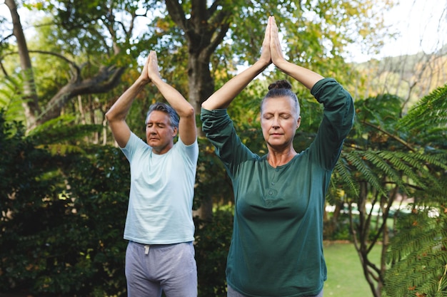 Gelukkig hoger kaukasisch paar dat yoga beoefent, mediteert in zonnige tuin. gezonde pensioenlevensstijl, tijd thuis doorbrengen.