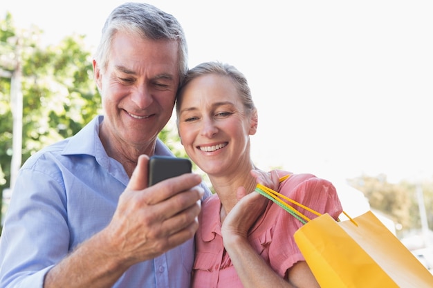 Foto gelukkig hoger paar die smartphoneholding het winkelen zakken bekijken