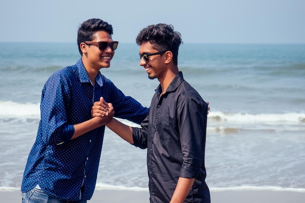 Gelukkig holi twee Indiase stijlvolle mans jonge vrienden knuffelen op het strand bij de zee. Langverwachte ontmoeting diwali van de broers in India Goa tropisch paradijs zomervakantie blauwe lucht en oceaan