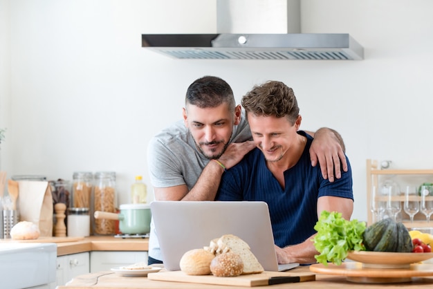 Gelukkig homoseksueel mannelijk paar die Internet samen thuis gebruiken