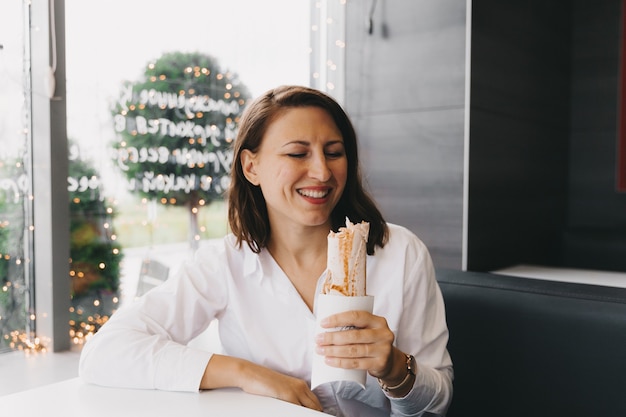 Gelukkig hongerig positief meisje, jonge vrouw die in een café zit en shoarma eet in pitabroodje