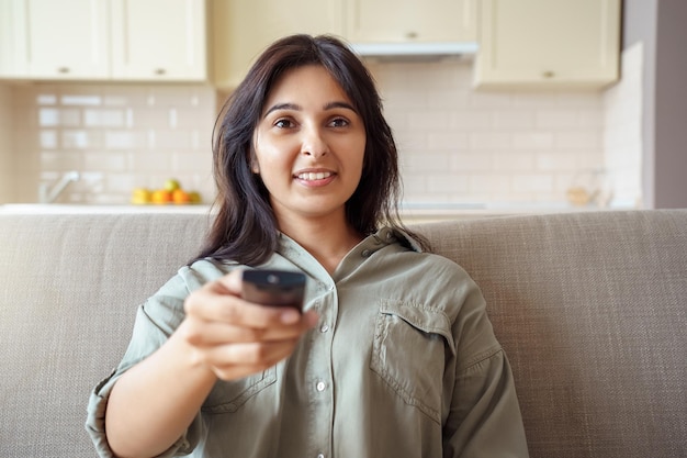 Foto gelukkig indiase vrouw zittend op de bank met afstandsbediening thuis tv kijken