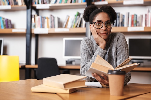 Gelukkig jong Afrikaans studentenmeisje dat bij de bibliotheek studeert, een boek leest