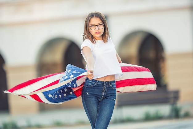 Gelukkig jong Amerikaans schoolmeisje vasthouden en zwaaien in de stad met de vlag van de V.S.