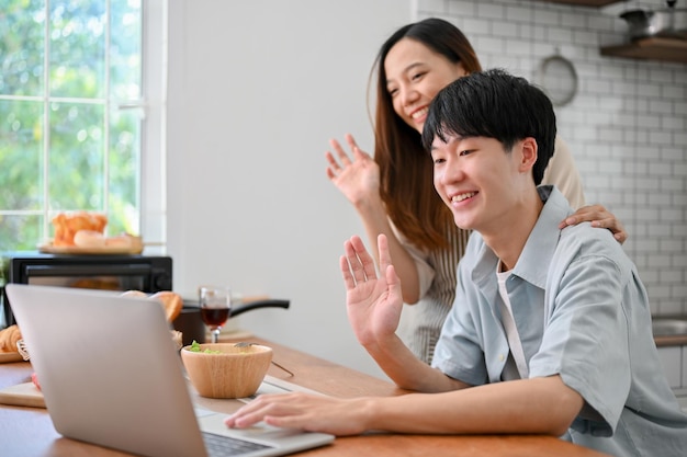 Gelukkig jong Aziatisch stel dat hun ouders gedag zegt via een videogesprek op een laptop in de keuken