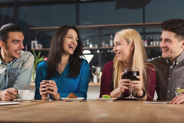 Gelukkig jong gezelschap van vrienden die koffie drinken en praten terwijl ze in een moderne coffeeshop zitten, kopieer ruimte.