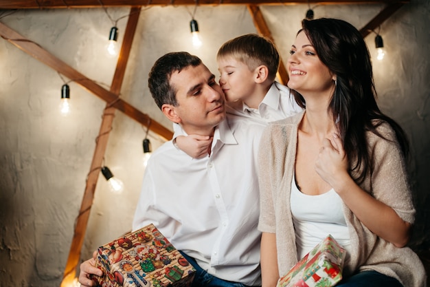 Gelukkig jong gezin in kerstversiering, moeder, vader en zoontje in de buurt van de kerstboom met cadeautjes in de buurt