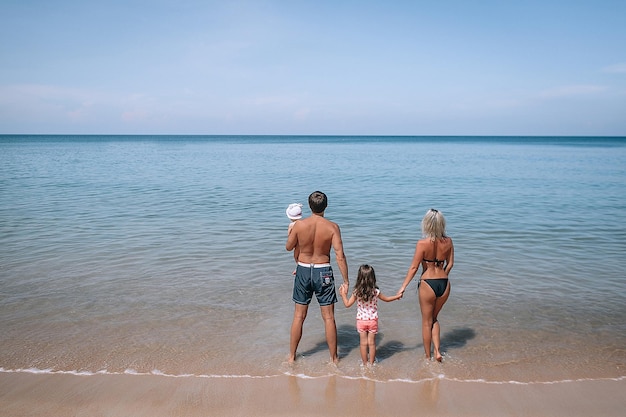 Gelukkig jong gezin in kleurrijke kleding kijken naar de zonsondergang op het strand. Gelukkige gezinslevensstijl. Achteraanzicht. Vakantie. Phuket. Thailand