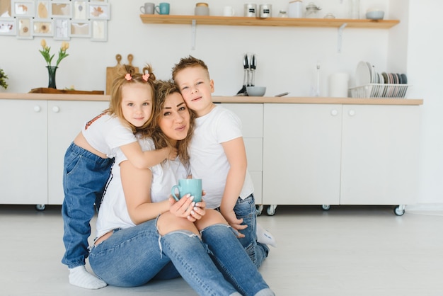 Gelukkig jong gezin, moeder met kleine kinderen zitten op de vloer in de keuken