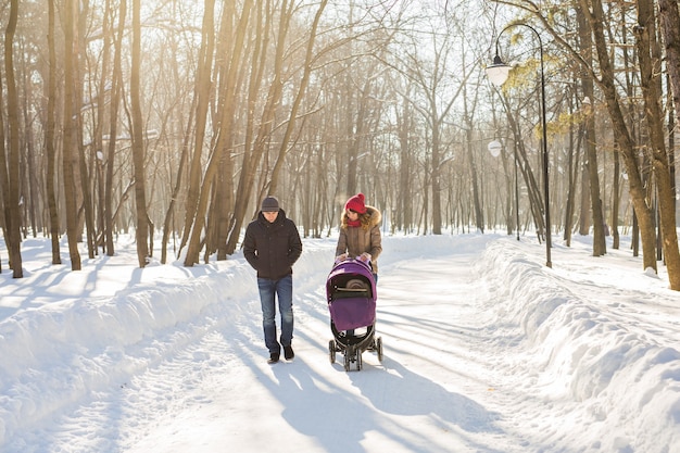 Gelukkig jong gezin wandelen in het park in de winter. De ouders dragen de baby in een kinderwagen door de sneeuw.